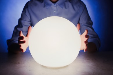 Businesswoman using glowing crystal ball to predict future at table in darkness, closeup. Fortune telling