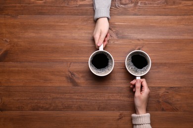 Women with cups of coffee at wooden table, top view. Space for text