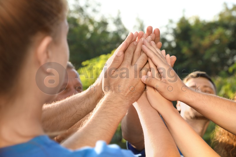 Group of volunteers joining hands together outdoors on sunny day