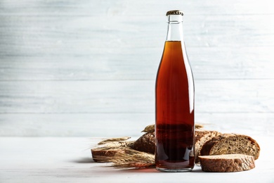 Photo of Bottle of delicious fresh kvass, spikelets and bread on white wooden table. Space for text