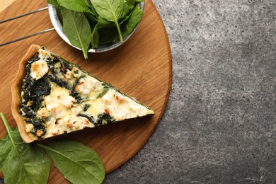 Photo of Piece of delicious homemade quiche and fresh spinach leaves on gray table, flat lay. Space for text