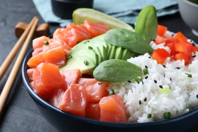 Delicious poke bowl with salmon, spinach and avocado served on black table, closeup