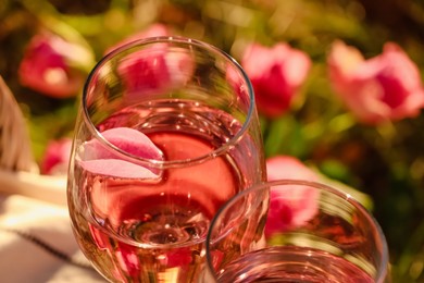 Photo of Glass of delicious rose wine with petals outside, closeup