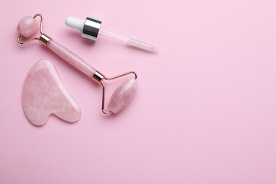 Photo of Gua sha stone, face roller and dropper on pink background, flat lay. Space for text