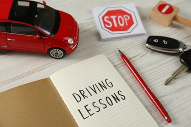Photo of Composition with workbook for driving lessons and toy car on white wooden background. Passing license exam