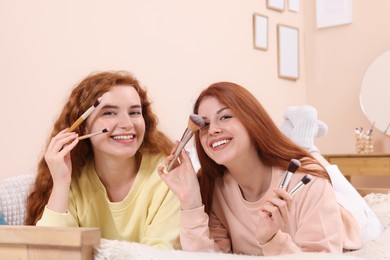 Photo of Portrait of beautiful young redhead sisters with makeup brushes at home