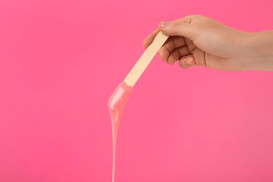Woman holding spatula with hot depilatory wax on pink background, closeup