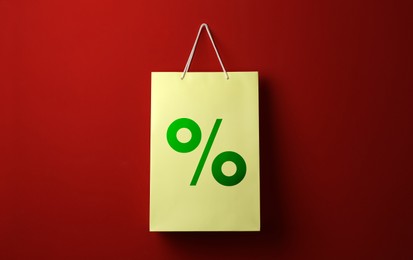Color paper shopping bag with percent sign hanging on red wall. Discount concept