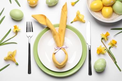 Festive Easter table setting with painted eggs and floral decor on white background, flat lay