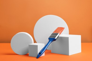 Scene with podium for product presentation. Figures of different geometric shapes and paint brush on orange background