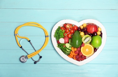 Heart shaped plate with fresh fruits, vegetables and stethoscope on wooden background, top view. Cardiac diet