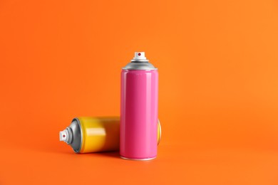 Colorful cans of spray paints on orange background. Space for text