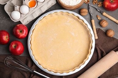Raw dough and ingredients for traditional English apple pie on grey table, flat lay