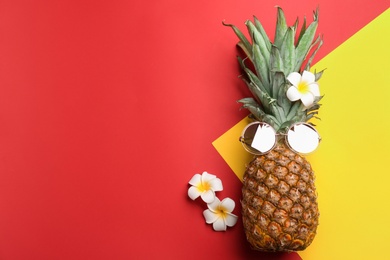 Top view of pineapple with sunglasses and flowers on color background, space for text. Creative concept