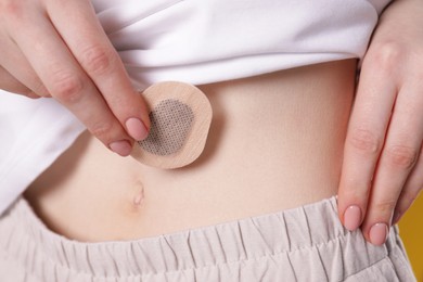 Photo of Woman applying contraceptive patch onto her belly on yellow background, closeup
