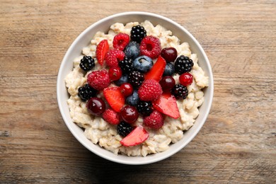 Photo of Bowl with tasty oatmeal porridge and berries on wooden table, top view. Healthy meal