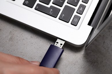 Man connecting usb flash drive to laptop at grey table, above view