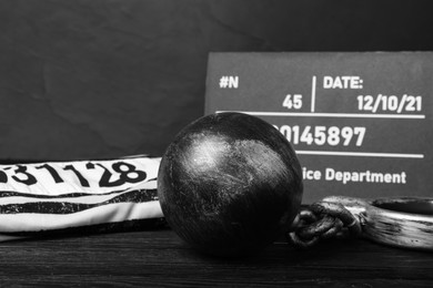 Metal ball with chain, prison uniform and mugshot letter board on black wooden table