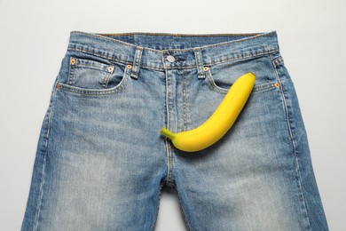 Men jeans with banana on light grey background, top view. Potency concept