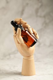 Photo of Bottle of organic cosmetic product in wooden mannequin hand on light marbled background