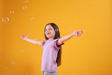 Photo of Little girl having fun with soap bubbles on yellow background