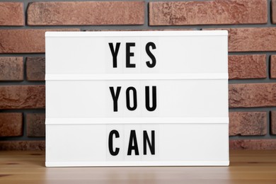 Lightbox with phrase Yes You Can on table against brick wall. Motivational quote