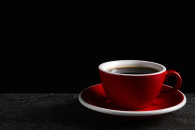 Photo of Red cup with aromatic coffee on black textured table. Space for text