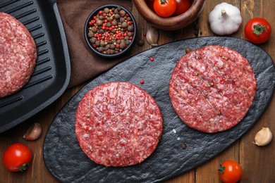 Raw hamburger patties with pepper and vegetables on wooden table, flat lay