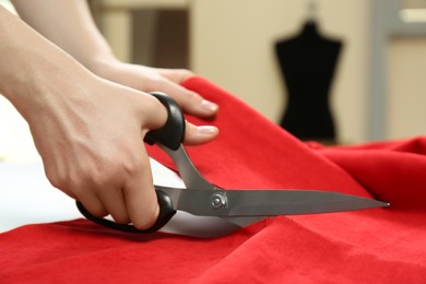Photo of Seamstress cutting red fabric with scissors at workplace, closeup