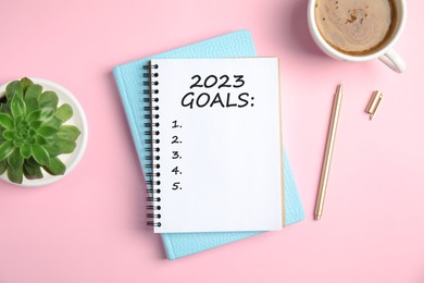 Notebook with inscription 2023 Goals, cup of coffee, plant and pen on pink background, flat lay. New Year aims 