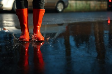 Photo of Woman with red rubber boots in puddle, closeup. Rainy weather