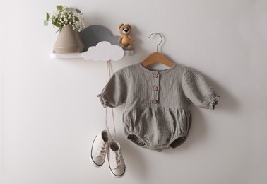 Cute children's baby onesie and shoes hanging on white wall