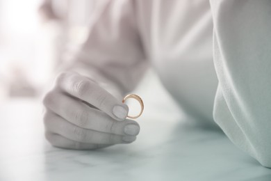 Woman holding wedding ring at table indoors, closeup. Cheating and breakup