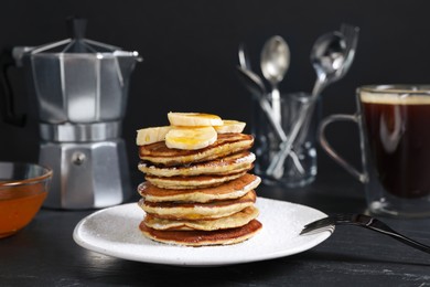 Plate of banana pancakes with honey and powdered sugar served on black table