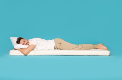 Smiling man lying on soft mattress against light blue background