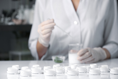 Scientist working in laboratory, focus on jars with different cosmetic products