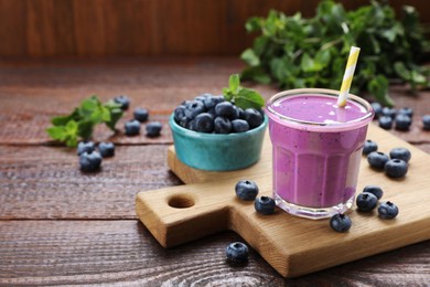 Photo of Glass of blueberry smoothie with mint and fresh berries on wooden table. Space for text