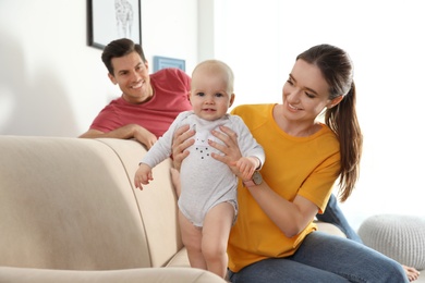 Happy parents with little baby on sofa in living room