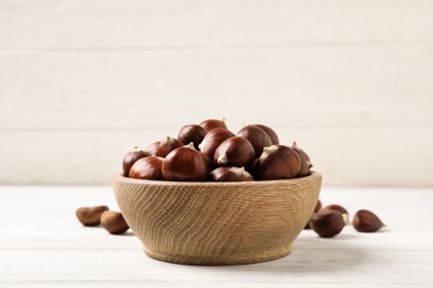 Photo of Fresh sweet edible chestnuts in bowl on white wooden table