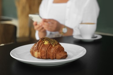 Woman sitting near tasty pastry and cup of aromatic coffee at black table in cafeteria, focus on croissant