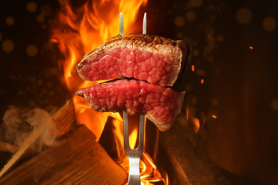 Carving fork with pieces of beef steak near bonfire