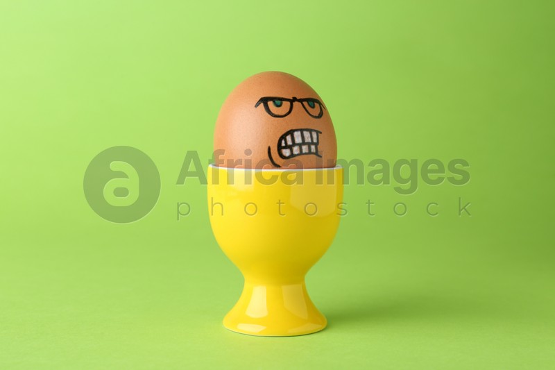 Egg with drawn angry face in cup on green background
