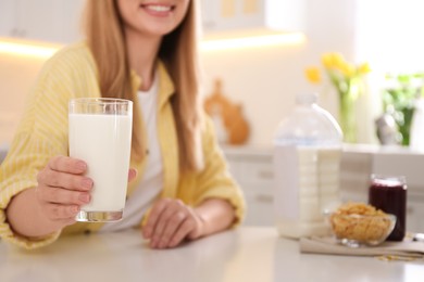 Young woman with gallon bottle of milk, glass and breakfast cereal at white table in kitchen, closeup