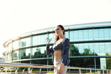 Young woman drinking water after running in city. Sports hydration