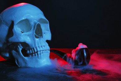 Photo of Human skull with pipe and smoke in neon lights on black background, closeup. Space for text