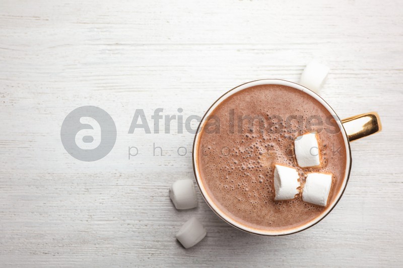 Cup of delicious hot cocoa with marshmallows on white wooden table, flat lay. Space for text
