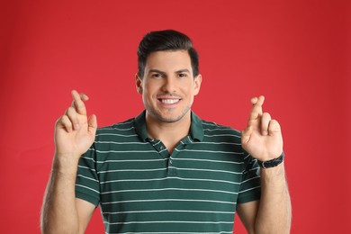 Man with crossed fingers on red background. Superstition concept