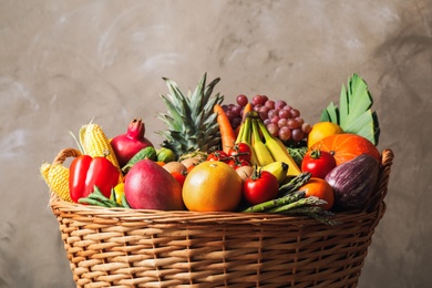 Assortment of fresh organic fruits and vegetables in basket on grey background, closeup