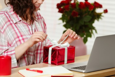 Photo of Valentine's day celebration in long distance relationship. Woman opening gift from her boyfriend indoors, closeup
