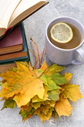 Yellow maple leaves, books and cup of tea on light gray table. Autumn atmosphere